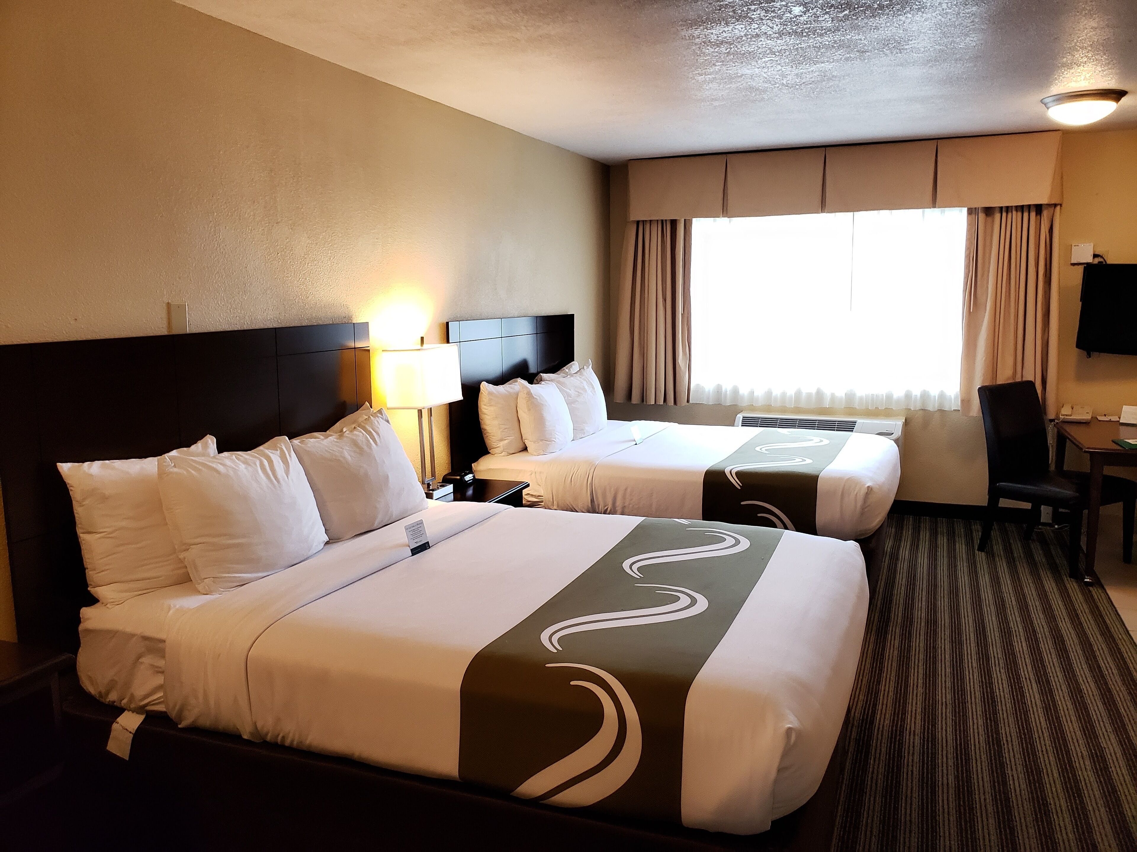 A hotel room with two beds, a desk, and a chair.