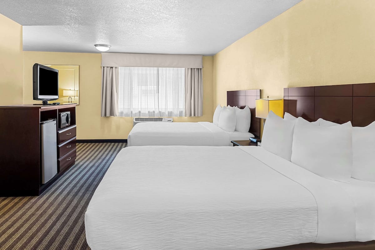 A hotel room with two beds, a desk with a television, and a window with curtains.