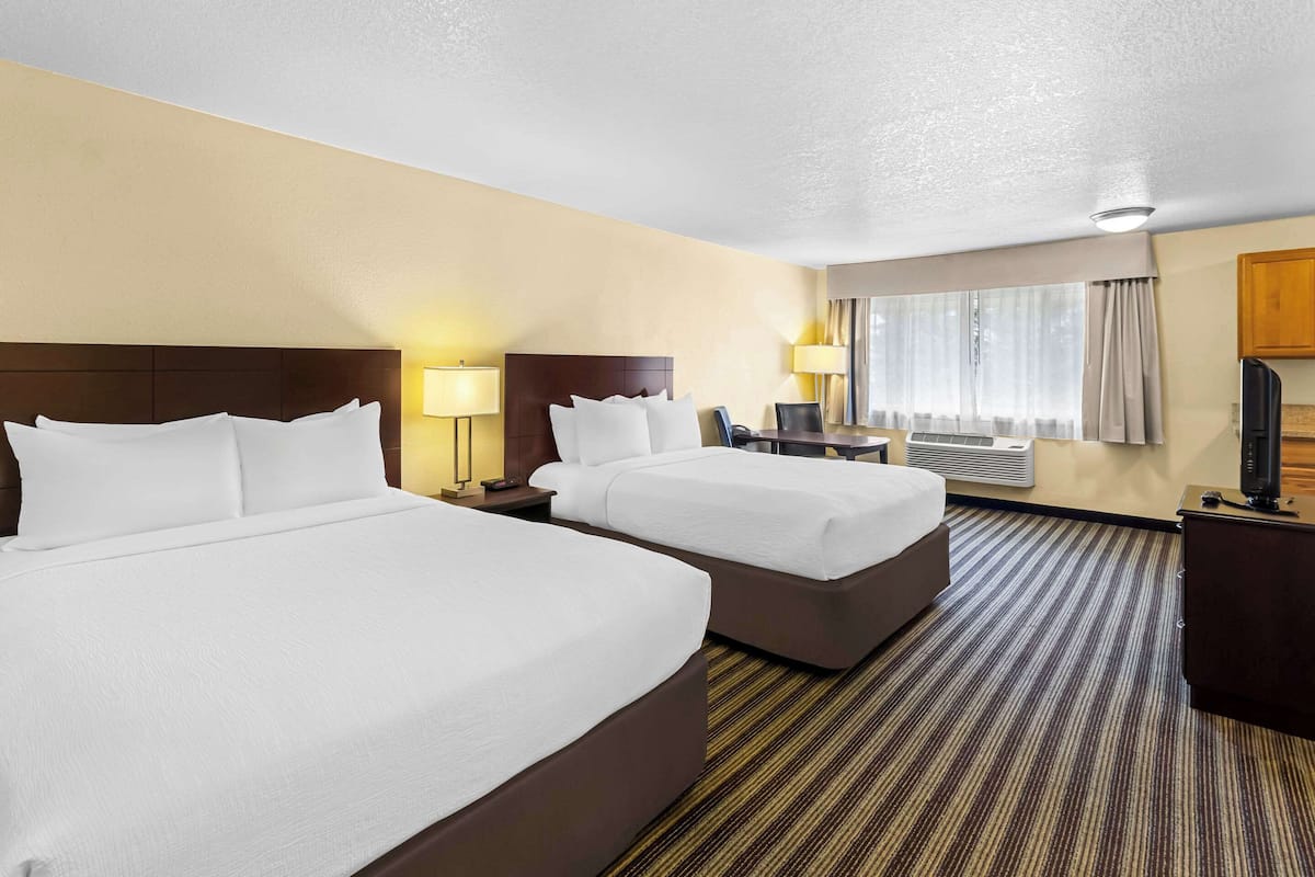 A hotel room with two beds, a desk, a chair, a TV, and a window with curtains.