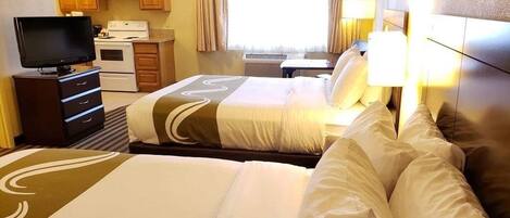 A hotel room with two beds, a television, a kitchenette, and a window with curtains.
