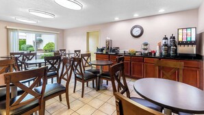 A restaurant with wooden chairs and tables, a kitchen area with a coffee machine, and a clock on the wall. - Quality Inn & Suites Vancouver - Hazel Dell (Vancouver)