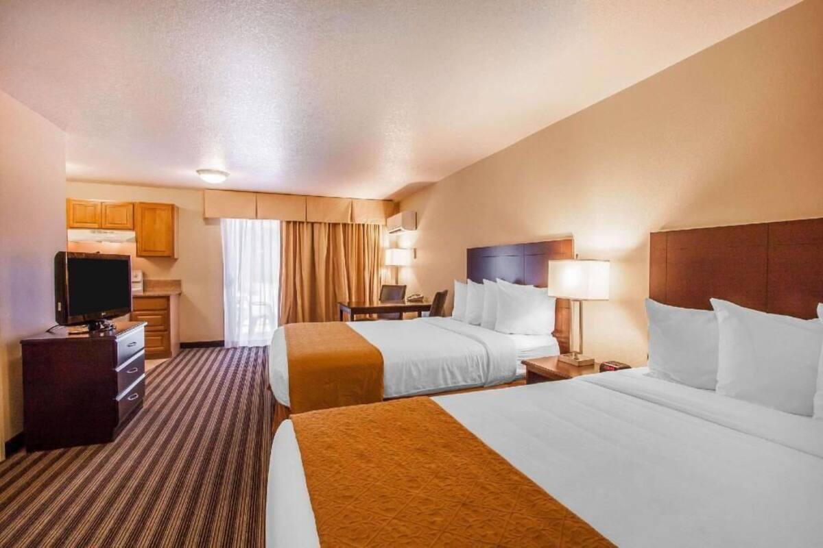 A hotel room with two beds, a desk, a television, and a bathroom visible in the background.