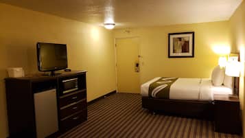 Una habitación de hotel con cama, escritorio, televisor, microondas y una puerta.