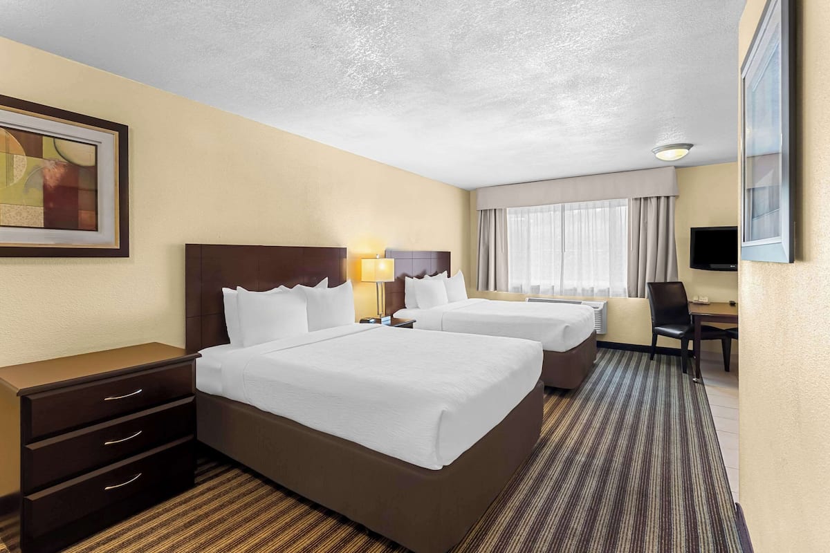 A hotel room with two beds, a desk, a chair, a TV, and a painting on the wall.