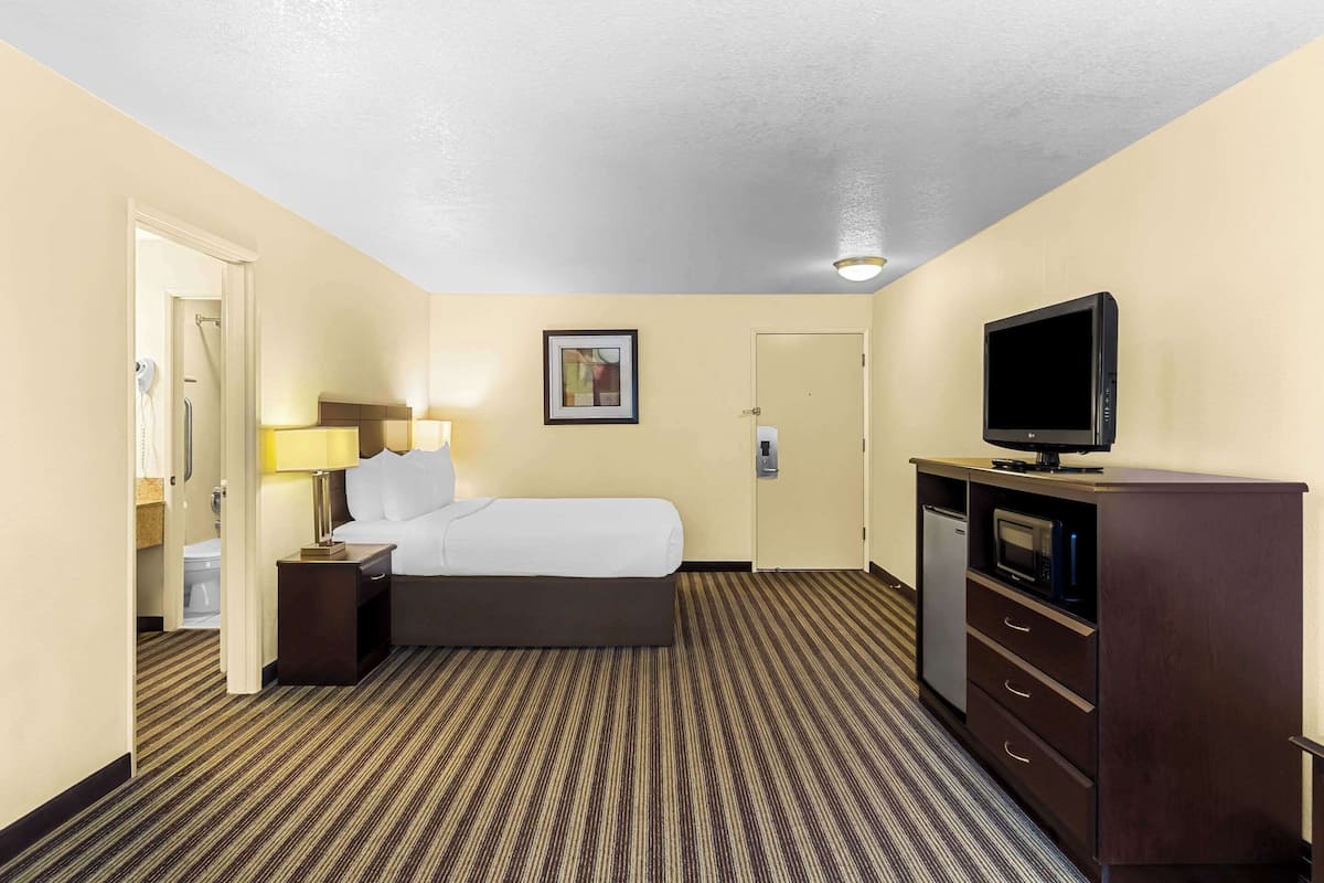 A hotel room with a bed, bedside table with lamp, TV, and a minibar.