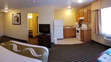 A hotel room with a bed, a desk, a television, a kitchenette, and a bathroom.