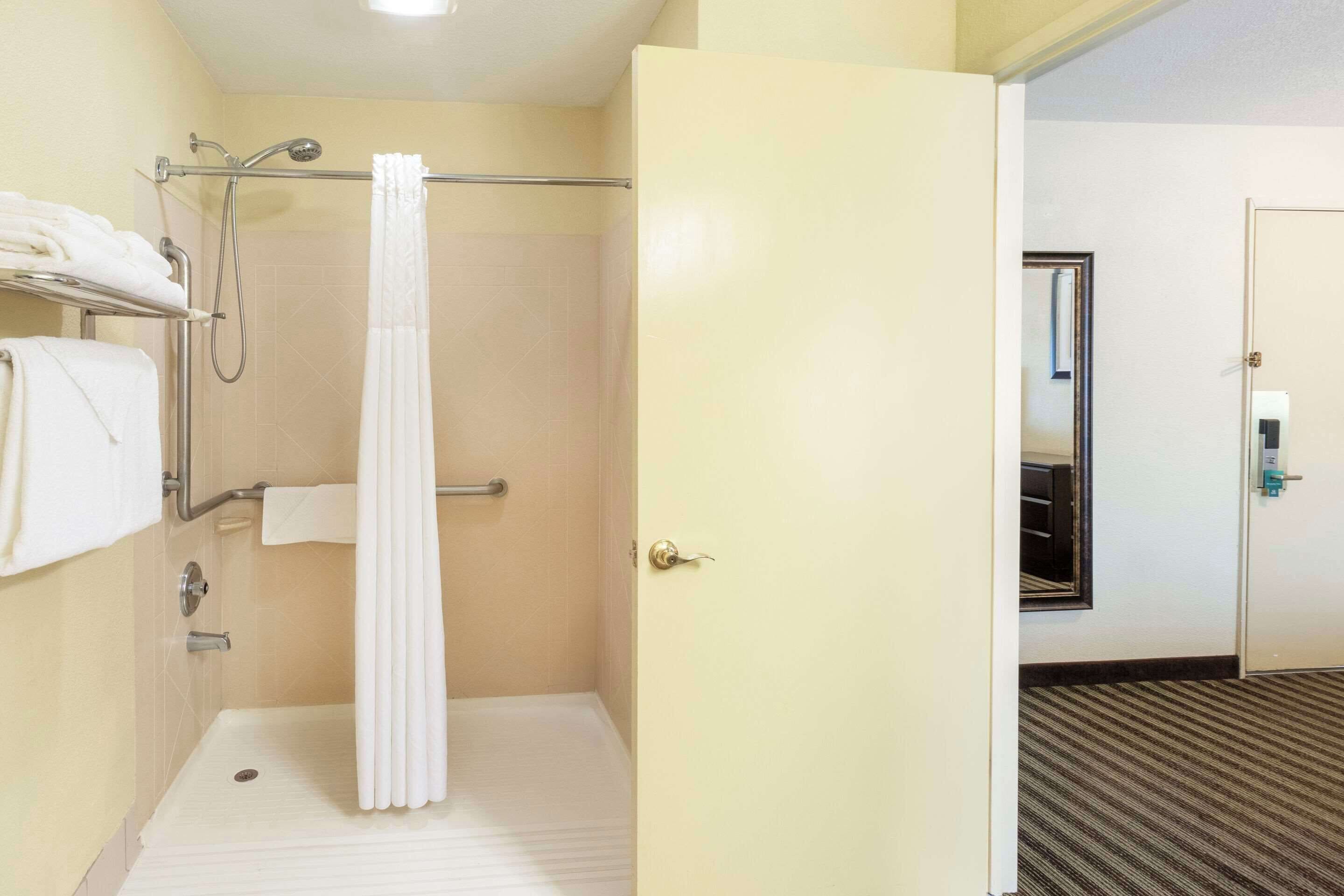 A hotel bathroom with a shower, a towel rack, and a door leading to another room.