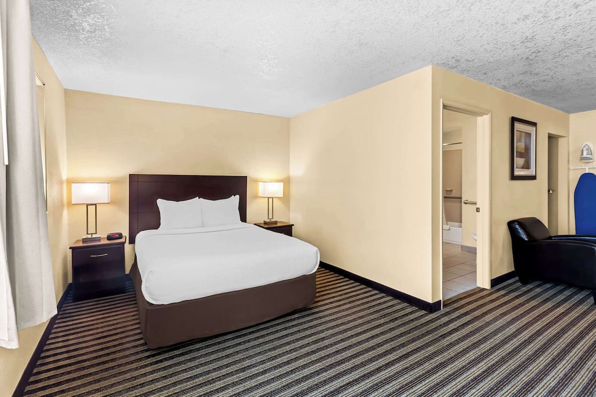 A hotel room with a large bed, two bedside tables with lamps, a chair, and a door leading to a bathroom.