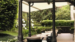 A covered outdoor seating area with tables and chairs, surrounded by lush greenery and a well-maintained garden. - Hotel Principe Di Savoia (Milan)
