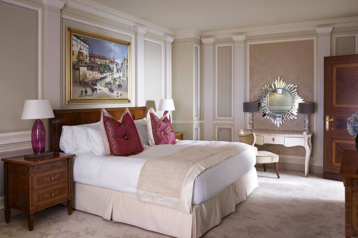 A well-appointed bedroom with a large bed, two bedside tables, a dresser, a mirror, and a framed painting on the wall.