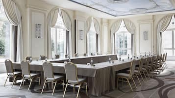 Un salón de conferencias amplio con una mesa larga, varias sillas y ventanas grandes.