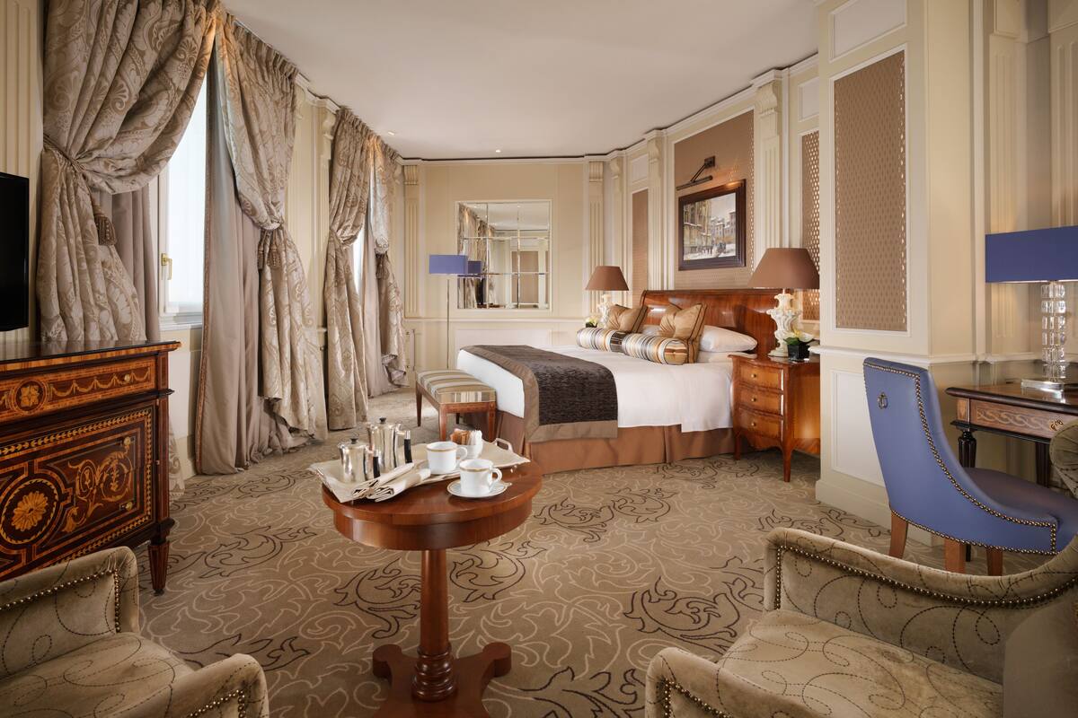 A hotel room with a large bed, a TV, a wooden dresser, a dining table, and a blue armchair.