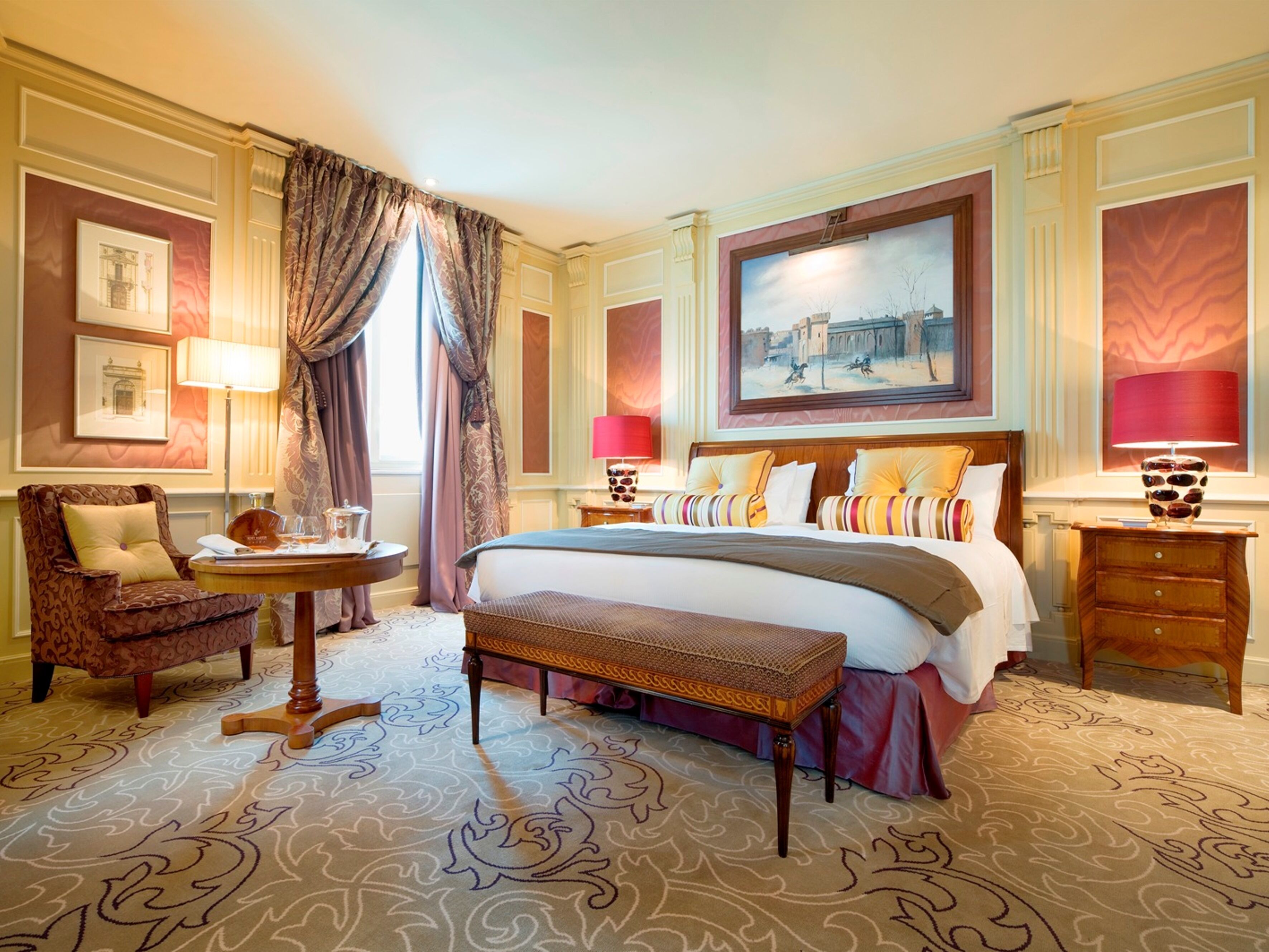 A spacious hotel room with a large bed, a sitting area with a chair and a small table, and a large window with curtains.