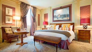 A spacious hotel room with a large bed, a sitting area with a chair and a small table, and a large window with curtains.
