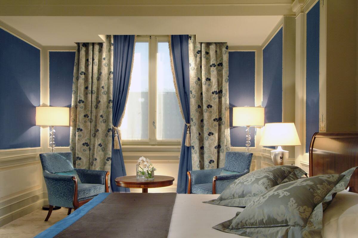 A hotel room with a bed, two armchairs, a small table, and two lamps.
