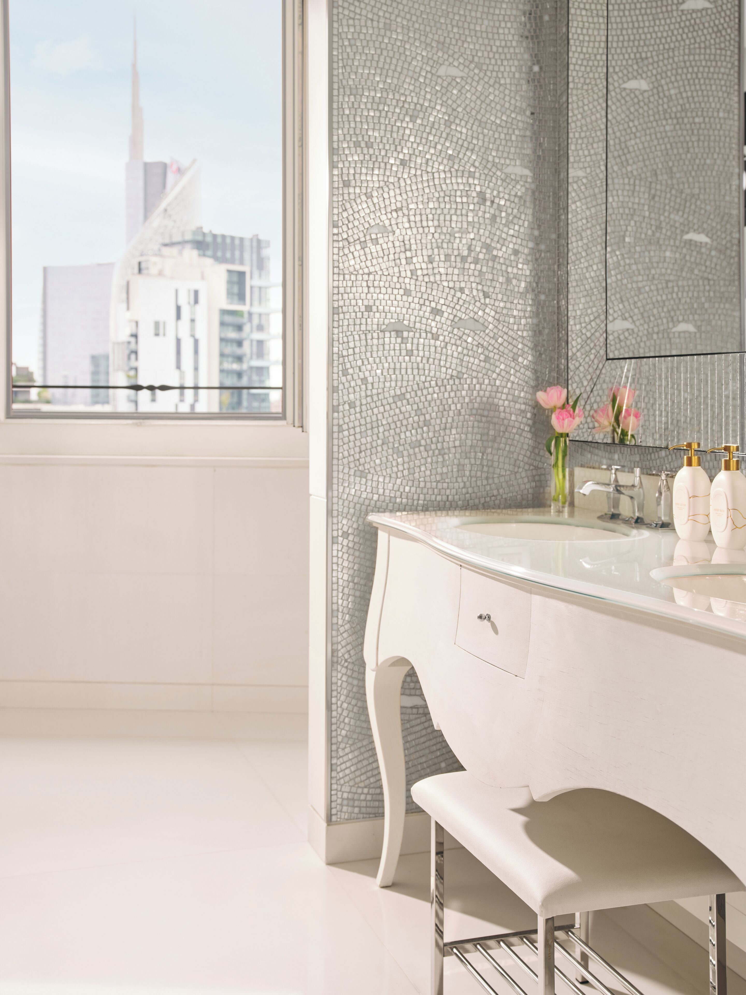 Een moderne badkamer met een grote spiegel, een witte wastafel en uitzicht op een hoog gebouw.
