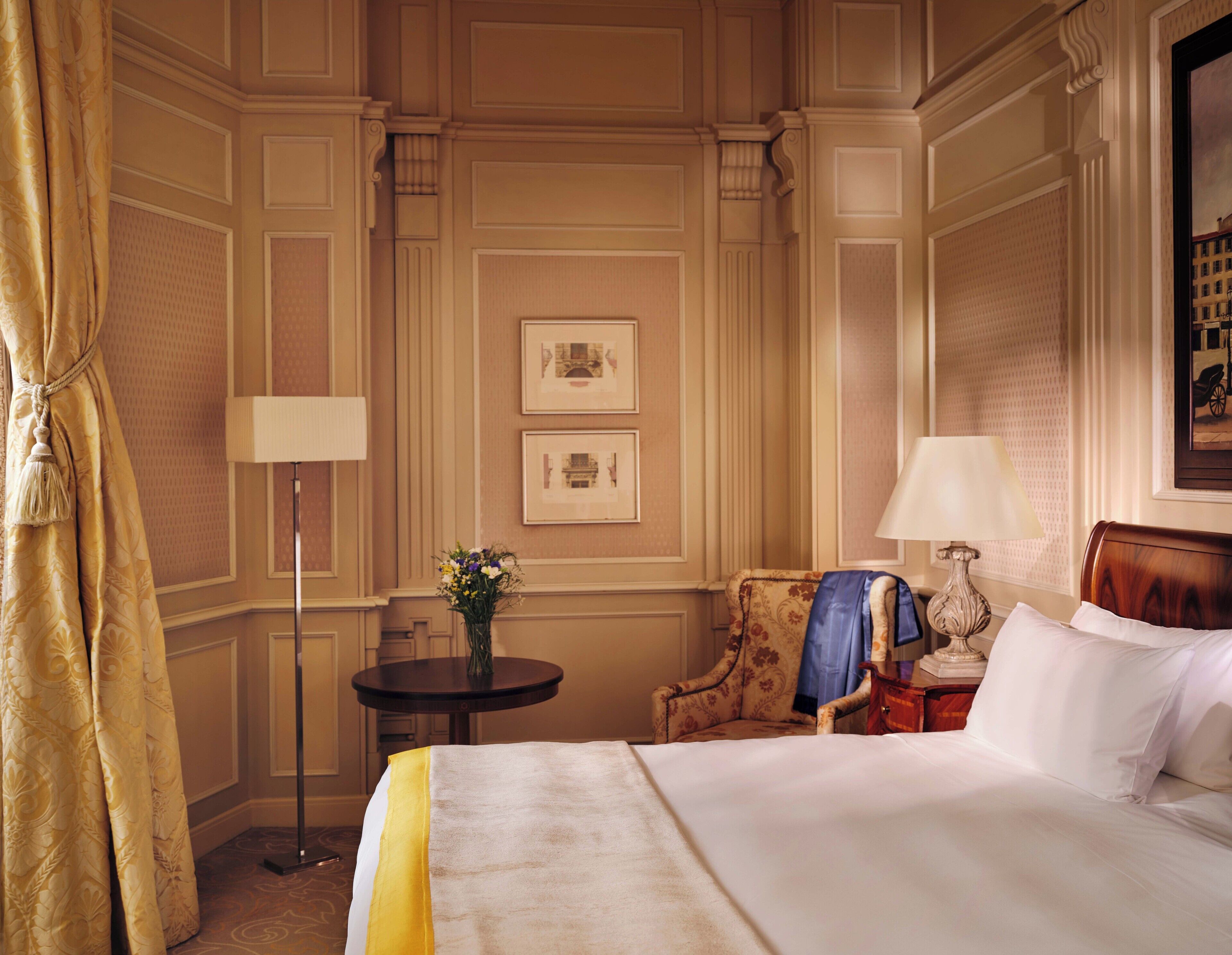 A hotel room with a bed, a chair, a small table, a lamp, and a picture on the wall.