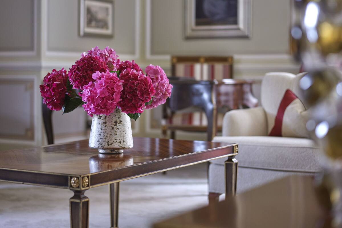 A room with a wooden coffee table, a white vase with pink flowers, a framed picture on the wall, and a white sofa with a red pillow.