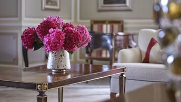 A room with a wooden coffee table, a white vase with pink flowers, a framed picture on the wall, and a white sofa with a red pillow.