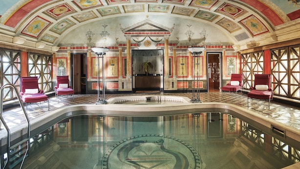 A luxurious indoor pool area with a central fountain, red and gold decorative elements, and a high ceiling with skylights. - Hotel Principe Di Savoia (Milan)
