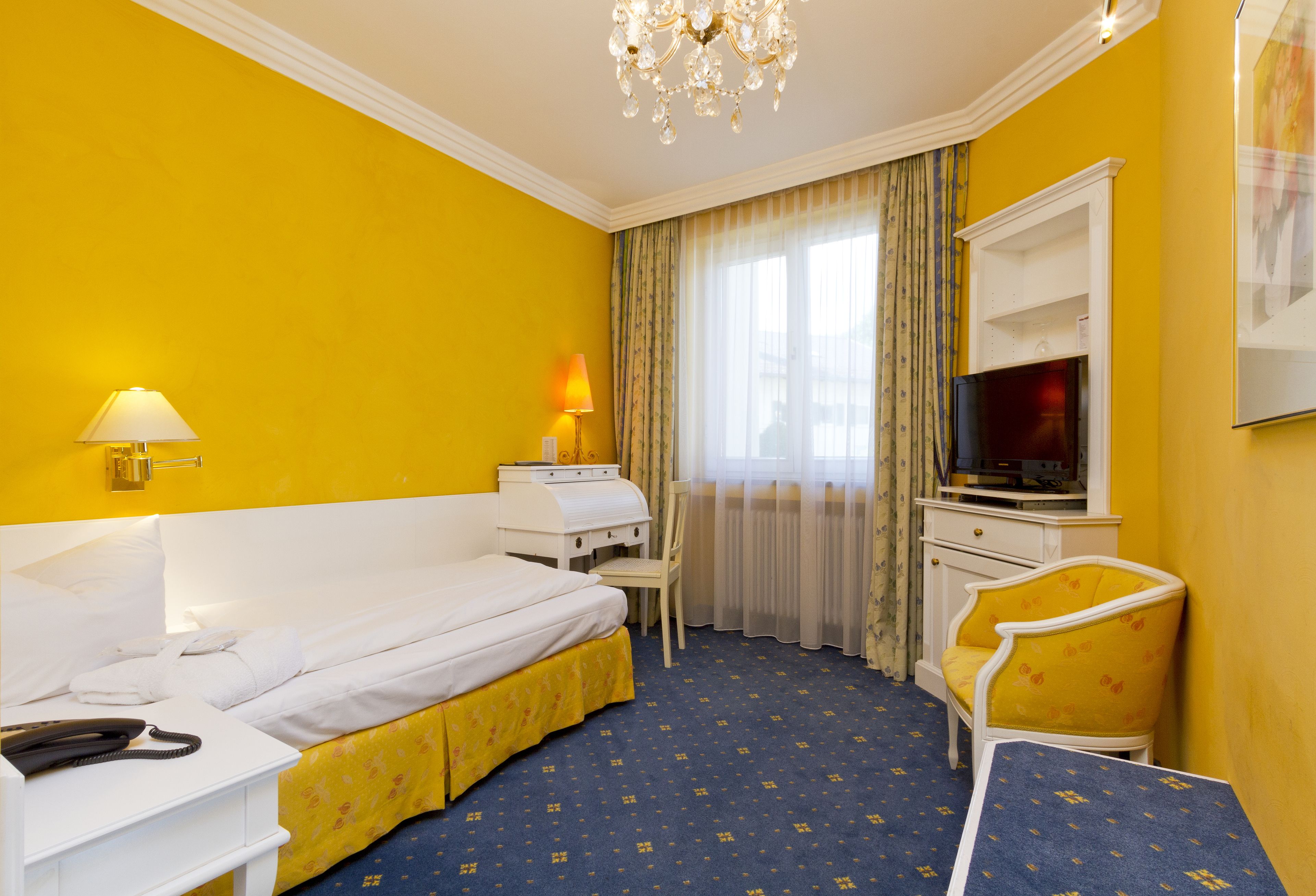 Ein Hotelzimmer mit Bett, Schreibtisch, Stuhl, Fernseher und einer Kandelaberleuchte.