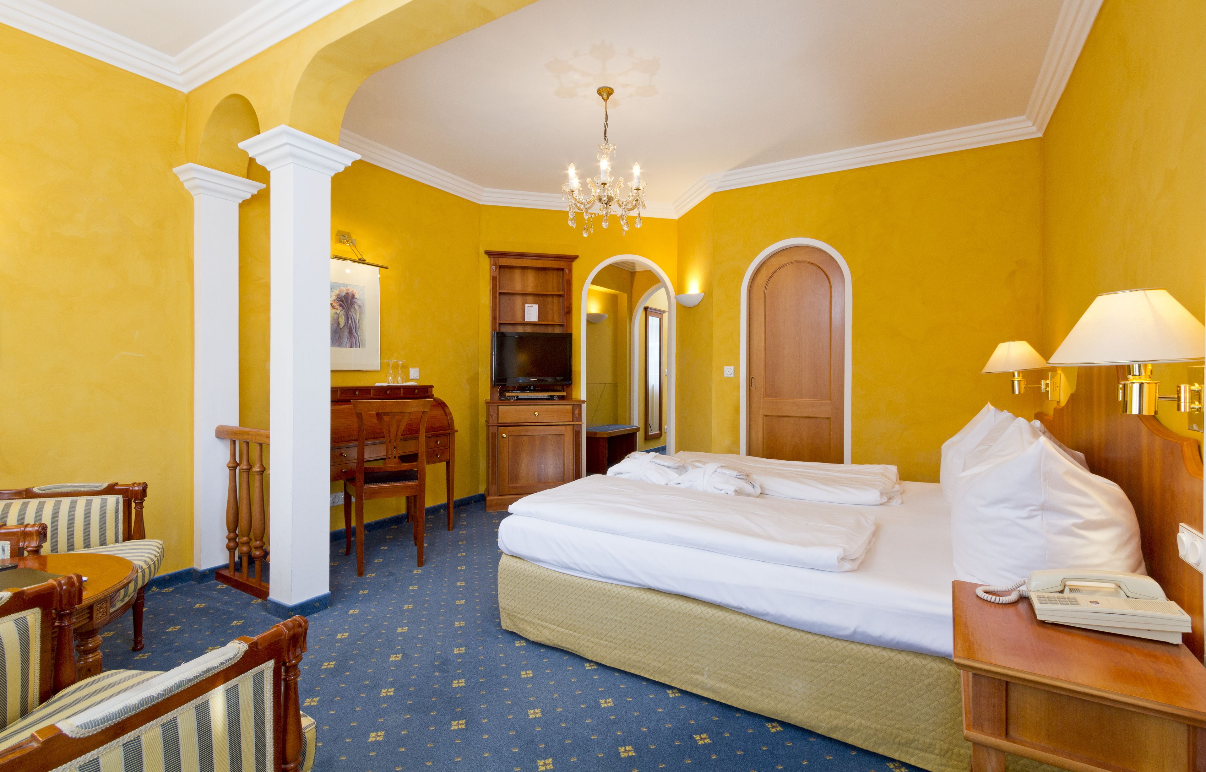 Een hotelkamer met een bed, een bureau, een stoel, een televisie en een kroonluchter.