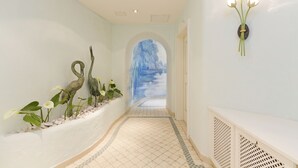 A hallway with a decorative wall featuring a swan sculpture, a wall-mounted light fixture with flowers, and a mural of a waterfall.