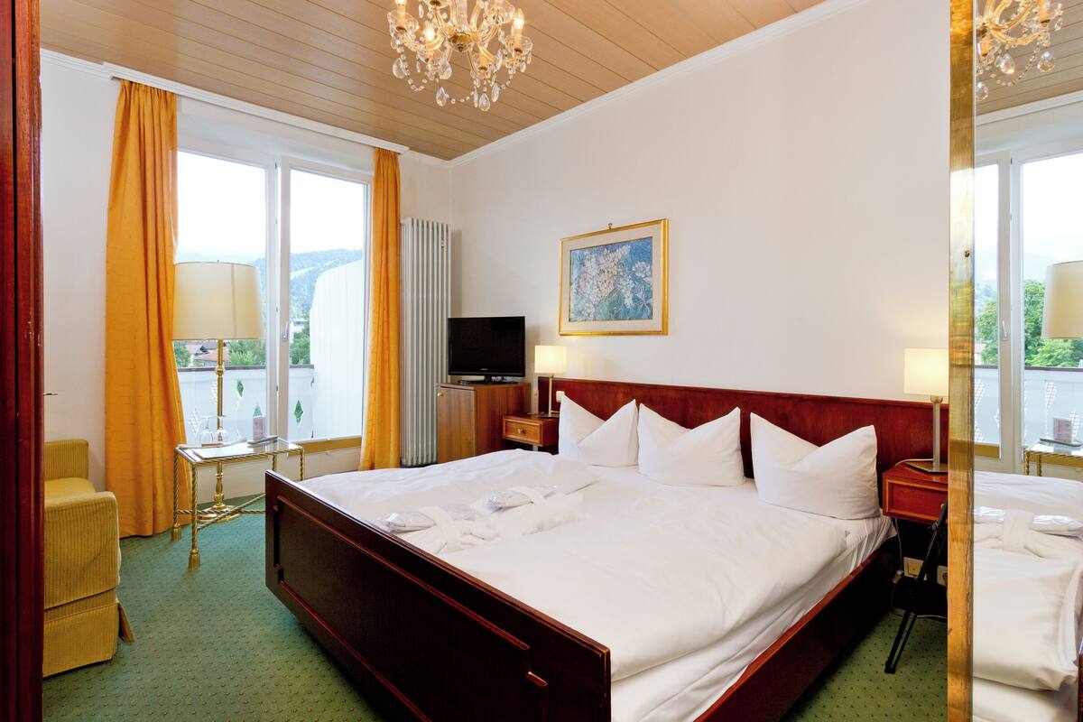 A hotel room with a large bed, a television, a painting, and a view of the outdoors.
