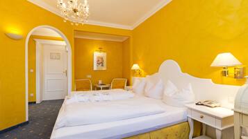 Habitación de hotel con una cama grande, un escritorio y una silla. Se ve una puerta que conduce a otra habitación y un cuadro en la pared.