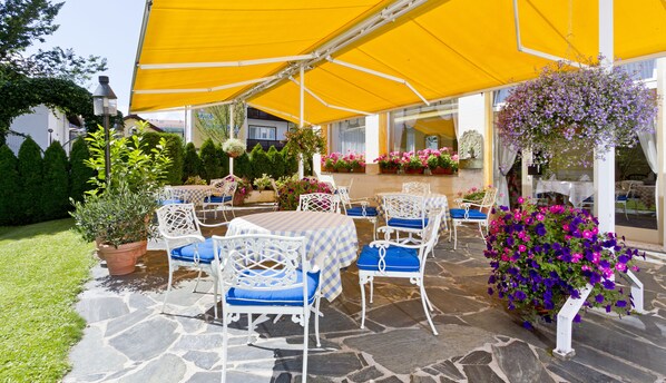 An outdoor patio with stone flooring, white wicker furniture, and yellow canopies. - Wittelsbacher Hof Swiss Quality Hotel (Garmisch-Partenkirchen)