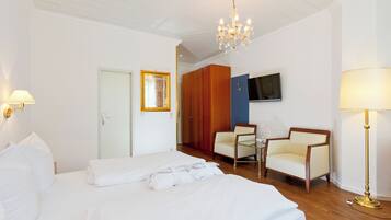 Ett hotellrum med en stor säng, två fåtöljer, en tv och en kristallkrona.