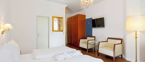 A hotel room with a large bed, two armchairs, a TV, and a chandelier.