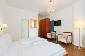 A hotel room with a large bed, two armchairs, a TV, and a chandelier. - Wittelsbacher Hof Swiss Quality Hotel (Garmisch-Partenkirchen)