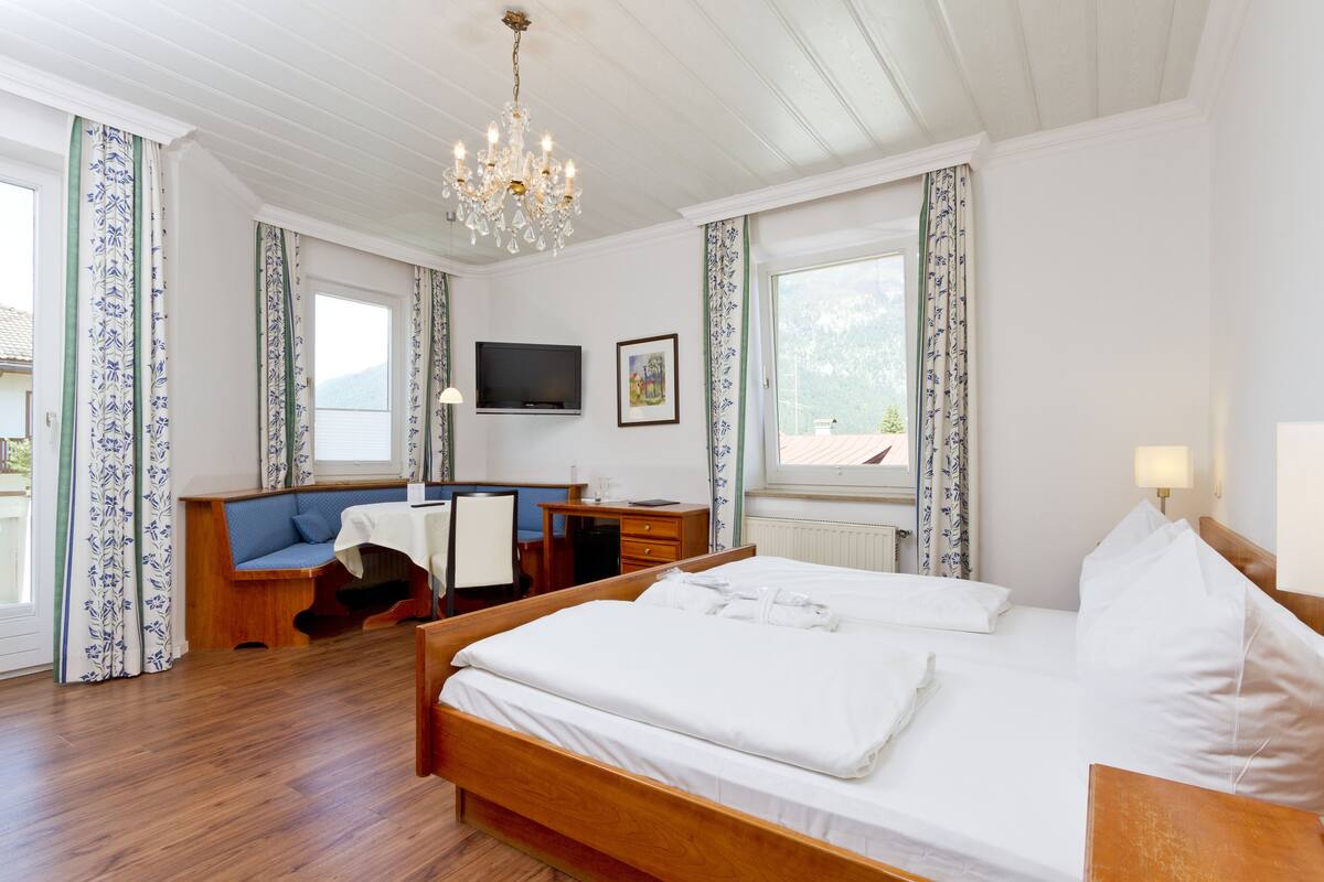 A hotel room with a wooden bed, a desk with a chair, a television, and a window with curtains.
