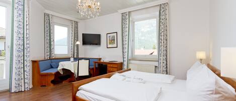 A hotel room with a wooden bed, a desk with a chair, a television, and a window with curtains.