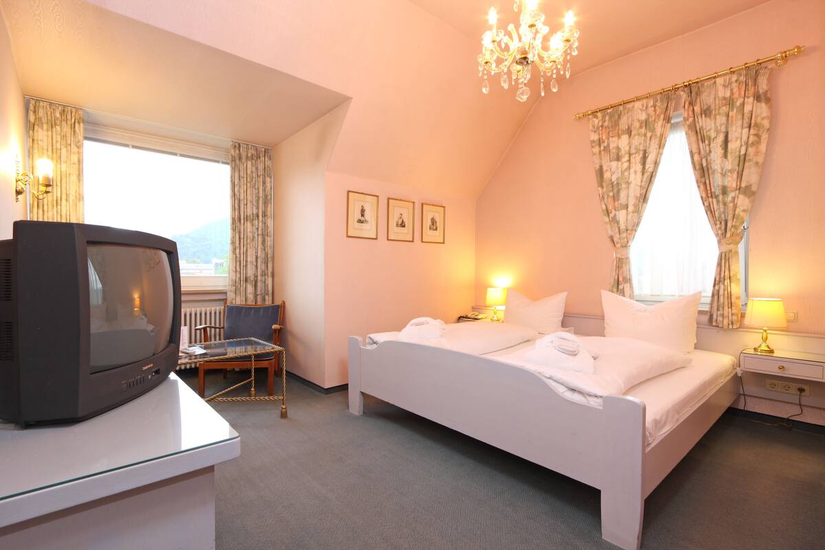 A hotel room with a bed, bedside table, lamp, and a television on a desk.