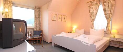 A hotel room with a bed, bedside table, lamp, and a television on a desk.