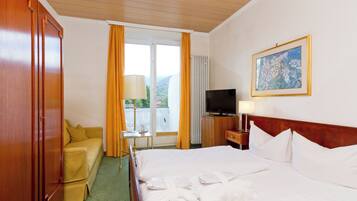 Habitación de hotel con cama, sofá, televisión, un cuadro y ventana con cortinas.