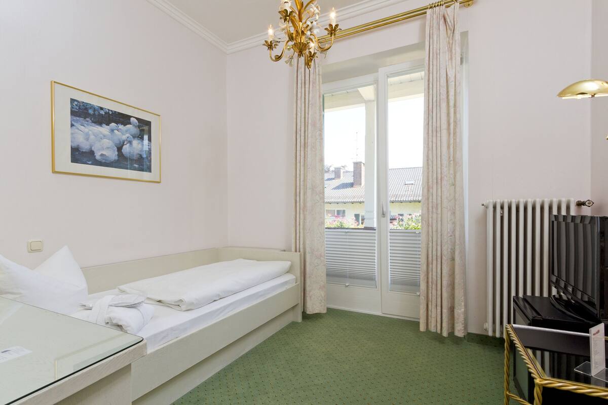 A hotel room with a bed, a small table, a TV, and a window with curtains.