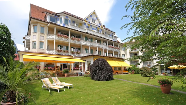 A hotel with a well-maintained lawn, outdoor seating, and a large decorative tree.