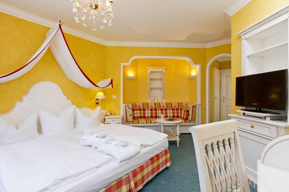 A hotel room with a large bed, a television, a sofa, and a dining table.