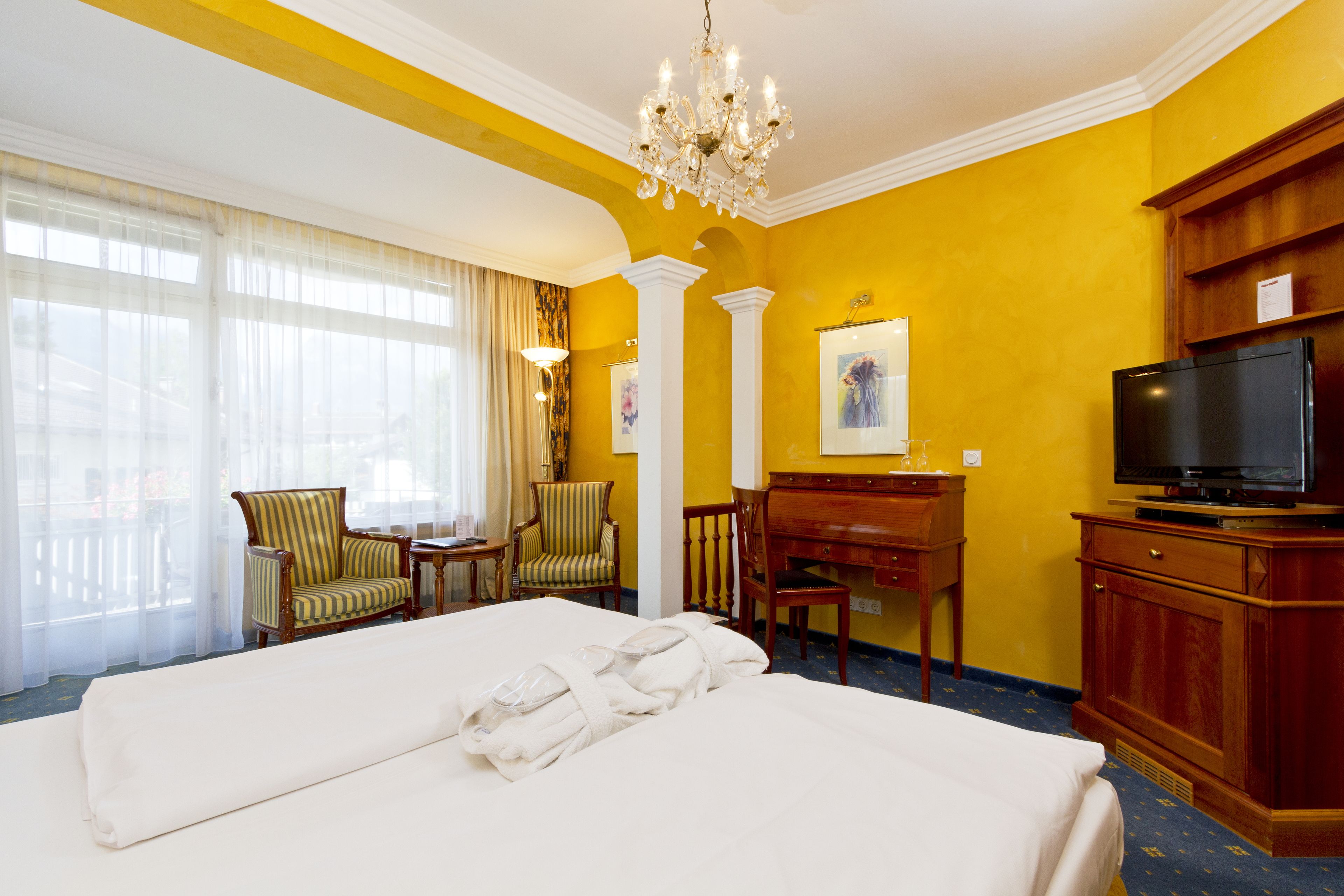 A hotel room with a large bed, a desk, a television, and a chandelier.