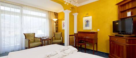 A hotel room with a large bed, a desk, a television, and a chandelier.