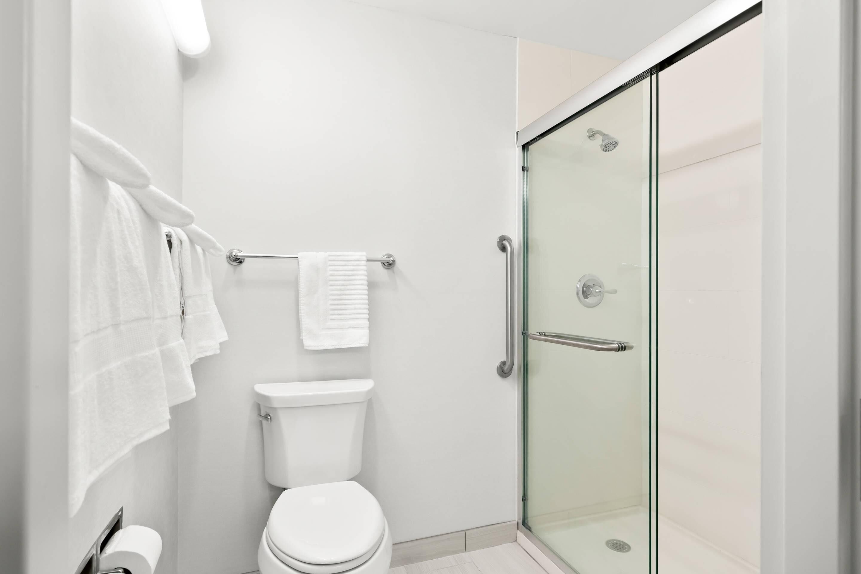 Un baño moderno con cabina de ducha de vidrio, inodoro blanco y toallero con varias toallas.