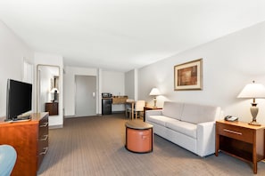 A hotel room with a television, sofa, coffee table, and a kitchenette.