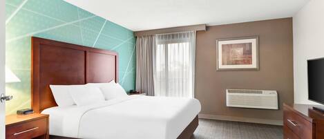 A hotel room with a bed, bedside table, lamp, air conditioning unit, and a television.