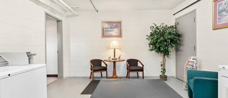 A conference room with a long table, two chairs, a desk with a lamp, a potted plant, and a bookshelf.