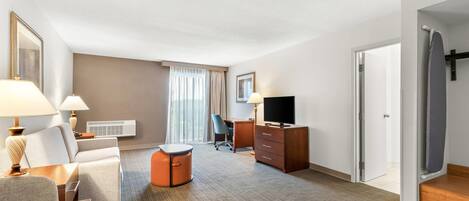 A hotel room with a sofa, a desk, a television, a chair, and a large window with curtains.