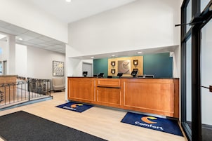 Zona de recepción con mostrador de madera, un escritorio con computadora y una puerta que da a otra habitación.