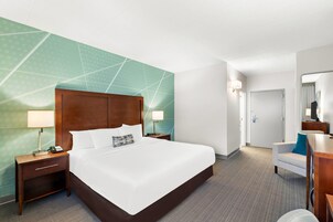 Una habitación de hotel con una cama grande, dos mesitas de noche, un escritorio, una silla y un espejo.